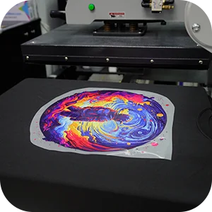 Heat press machine with a colorful DTF transfer film positioned on a black t-shirt.
