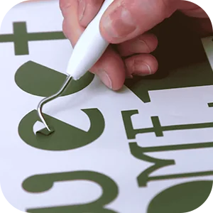 Close-up of a hand using a weeding tool to remove excess vinyl from a design.